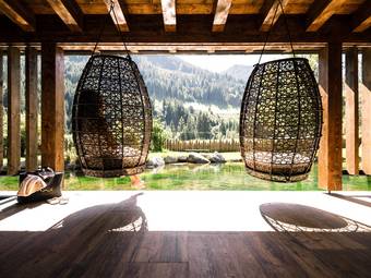 Peace in your own rhythm Two large hanging chairs made of woven rattan overlooking a natural pond and forested mountains in the background.